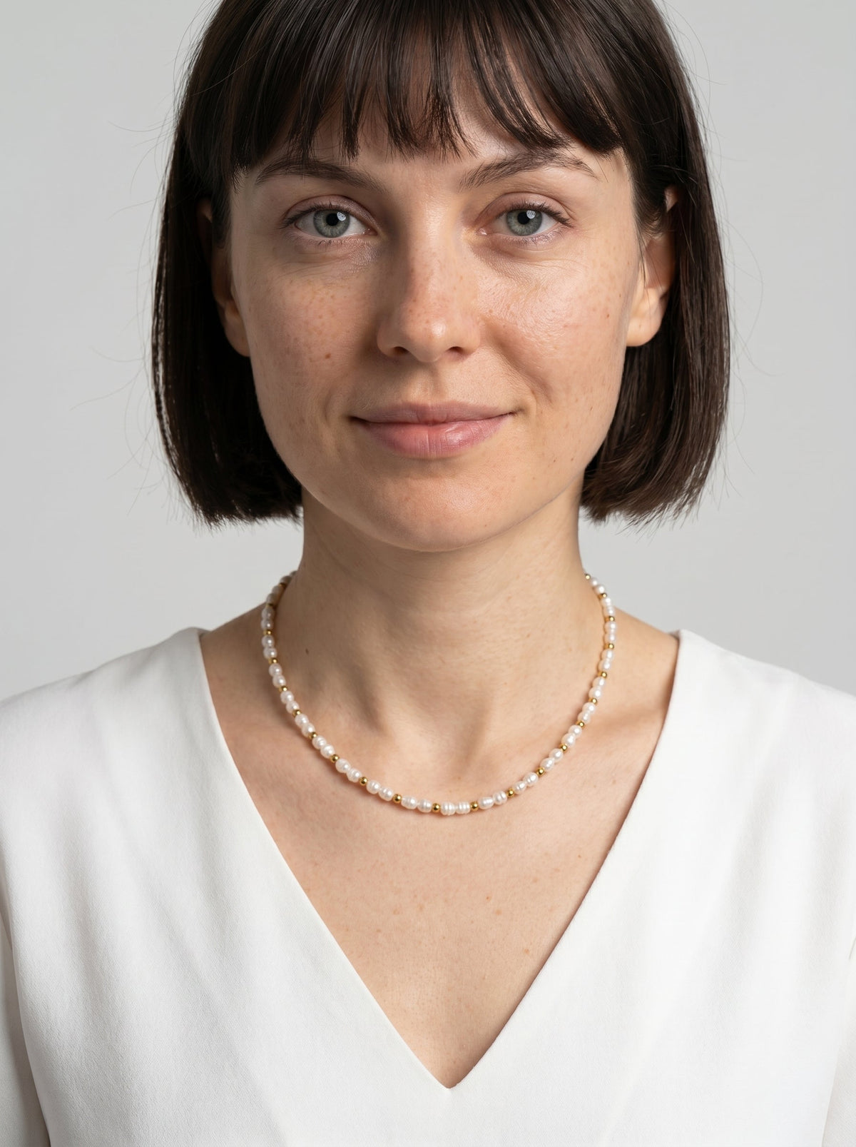 Delikatny naszyjnik z białymi naturalnymi perłami i złotymi detalami, noszony przez modelkę, tworzący elegancki, minimalistyczny i wyrafinowany wygląd.