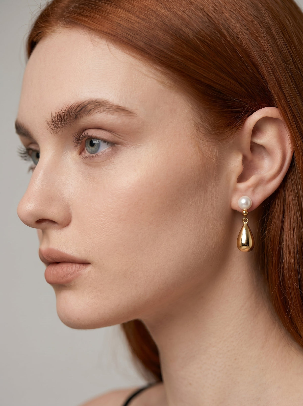 Złoty wiszący kolczyk z białą perłą i metalową kroplą noszony przez modelkę