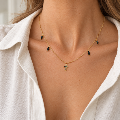 Naszyjnik z krzyżykiem i czarnymi kroplami — biżuteria podczas noszenia, kadr bez twarzy, w złotym odcieniu.