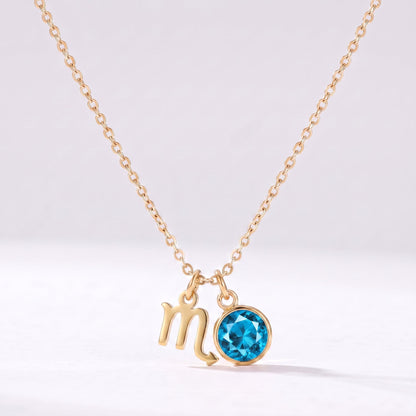 Złoty naszyjnik ze znakiem zodiaku Skorpiona i kamieniem urodzeniowym niebieskim topazem.