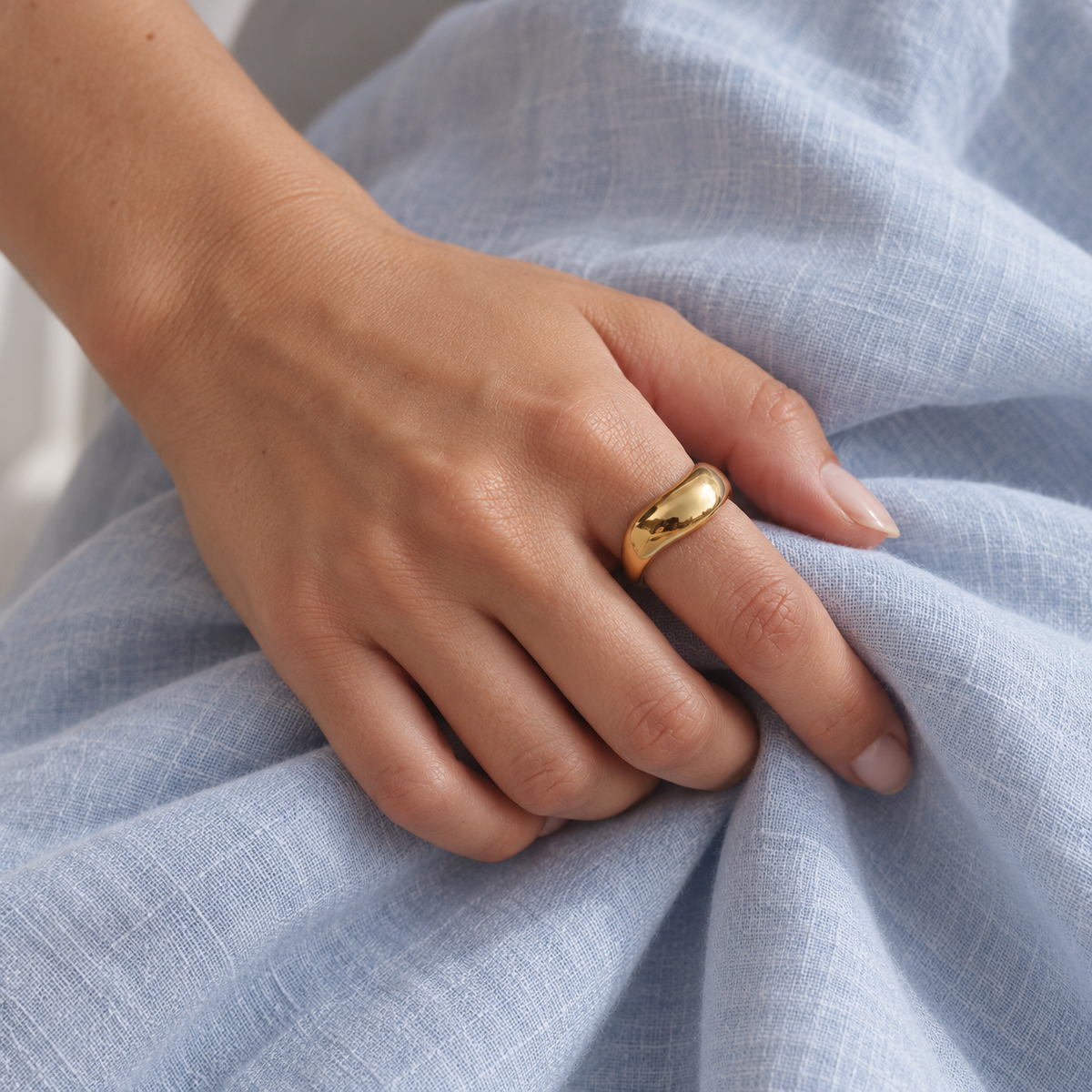 Pozłacany pierścionek o falującej formie — zdjęcie na osobie, kadr bez twarzy, wykończenie w kolorze złota.