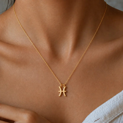 Złoty naszyjnik ze znakiem Ryb — symbol zodiaku, noszony przez modelkę.