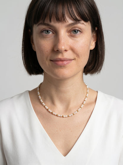 Delikatny naszyjnik z białymi naturalnymi perłami i złotymi detalami, noszony przez modelkę, tworzący elegancki, minimalistyczny i wyrafinowany wygląd.